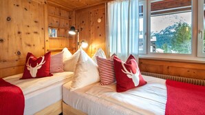 Quarto de cabana de madeira com duas camas, uma janela com vista e uma estante com livros.