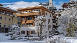 Um edifício de vários andares com fachada de madeira, uma torre do relógio e paisagem coberta de neve.