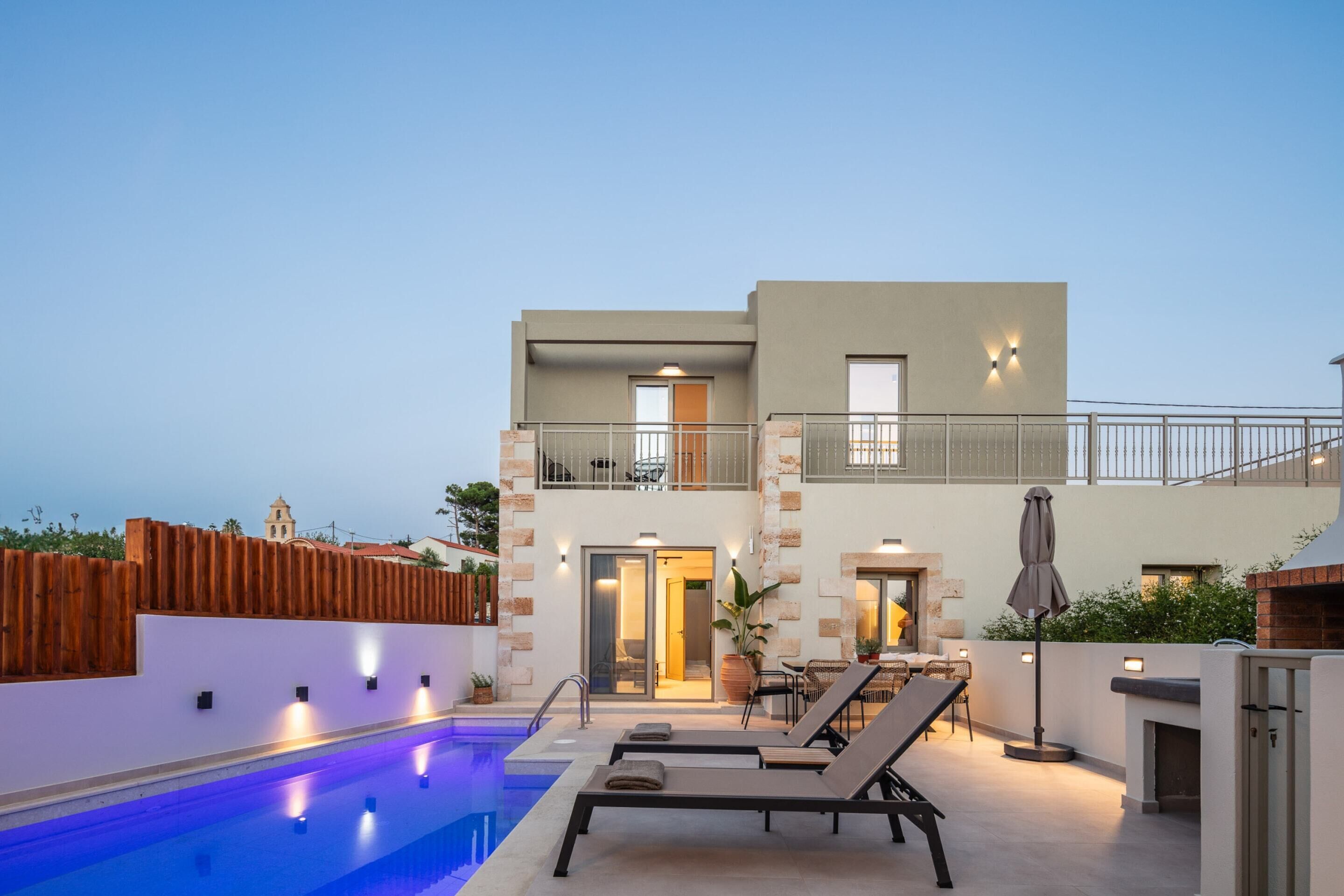 A modern two-story building with a swimming pool, lounge chairs, and a barbecue area.