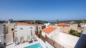 Uma área de piscina no terraço, com espreguiçadeiras, piscina e vista para o mar e edifícios ao redor.