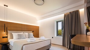 Quarto de hotel moderno com uma cama grande, mesas de cabeceira, uma pequena mesa e uma janela com cortinas.