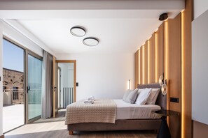 A modern bedroom with a bed, bedside table, and a view through a glass door to an outdoor area. - Marvelous new Luxury Villa With Heated Pool! (Rethymno)