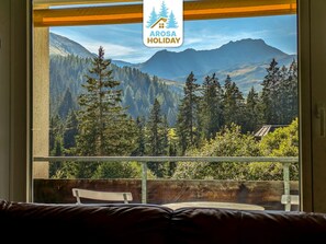 A window with a view of a forested mountain landscape, a wooden bench, and a sign reading 'Arosa Holiday'. - Rothornblick 44 by Arosa Holiday Appartement/Fewo,   Schöne 2½-Zimmerwohnung by Interhome (Arosa)
