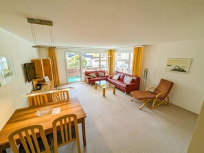 A furnished living room with a dining area, a red sofa, a wooden dining table, and a chair. - Rothornblick 44 by Arosa Holiday Appartement/Fewo,   Schöne 2½-Zimmerwohnung by Interhome (Arosa)