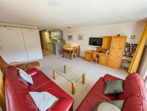 A compact living space with a red sofa, a glass coffee table, a dining area, and a kitchen with wooden cabinets. - Rothornblick 44 by Arosa Holiday Appartement/Fewo,   Schöne 2½-Zimmerwohnung by Interhome (Arosa)