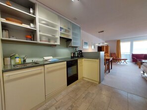 A modern kitchen with a dishwasher, oven, and a dining area with a table and chairs. - Rothornblick 44 by Arosa Holiday Appartement/Fewo,   Schöne 2½-Zimmerwohnung by Interhome (Arosa)