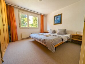 A bedroom with a bed, a nightstand, a painting on the wall, and a window with curtains. - Rothornblick 44 by Arosa Holiday Appartement/Fewo,   Schöne 2½-Zimmerwohnung by Interhome (Arosa)