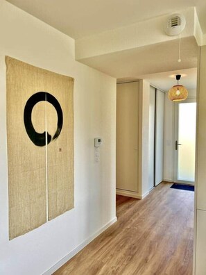 Een gang met een houten vloer, een wandlamp en een deur aan het einde.