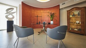 A modern interior with two grey chairs, a glass table, a potted plant, and a wooden cabinet with glass doors.