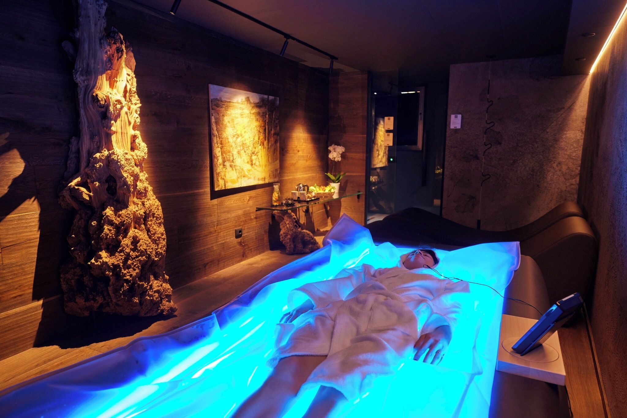 A massage therapy room with a wooden wall, a rock sculpture, and a massage table with a person lying on it.