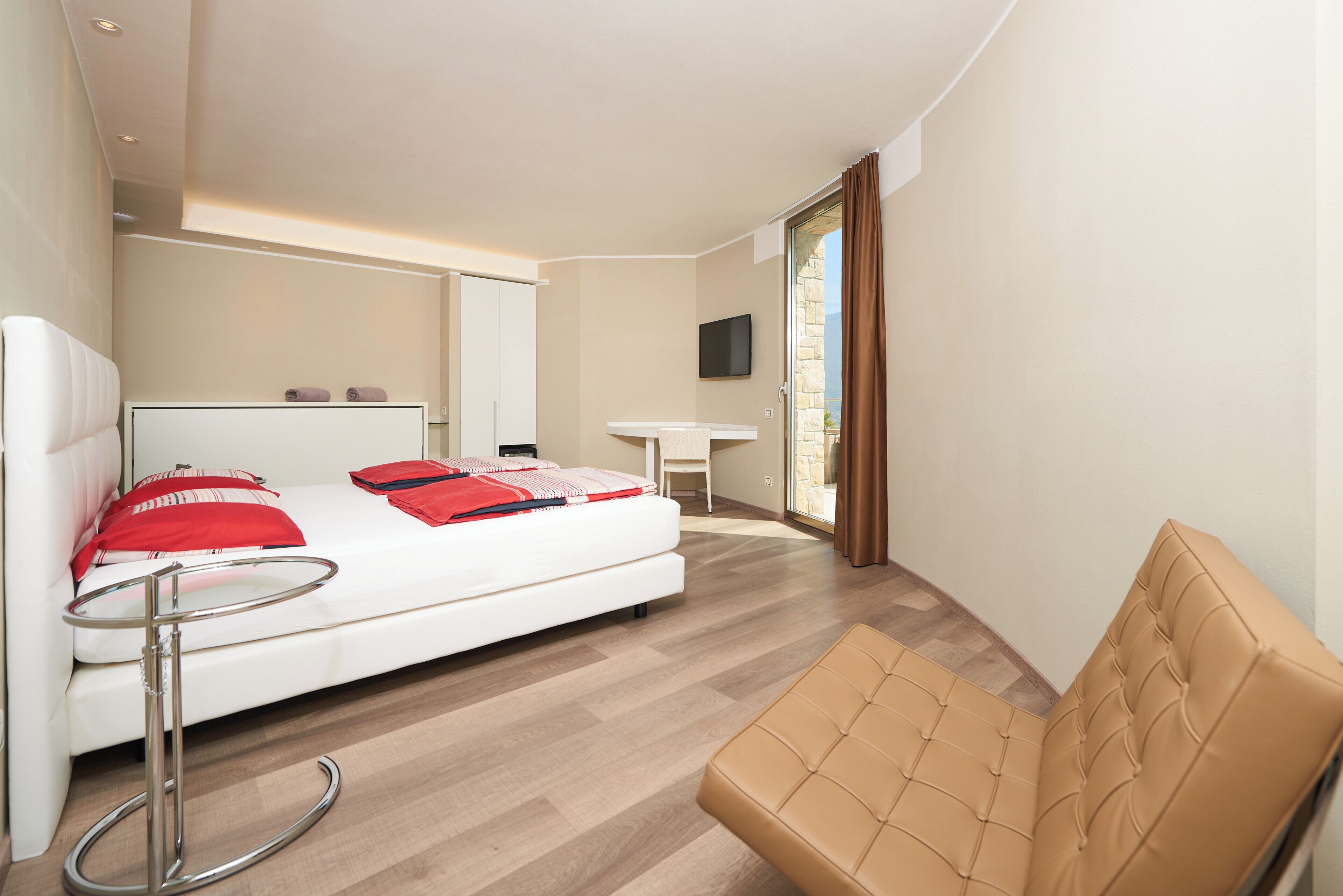 A modern hotel room with a bed, a desk, a chair, and a TV.