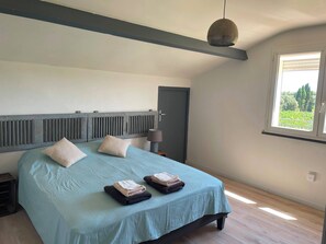Ein Schlafzimmer mit Bett, Kissen, einer Nachttischlampe, einem Fenster und Blick ins Grüne.