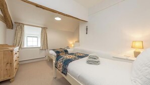 A bedroom with a bed, bedside table, lamp, window, and wooden dresser.