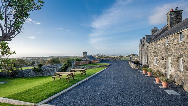 A stone building with a gravel driveway, picnic tables, and a stone wall.
