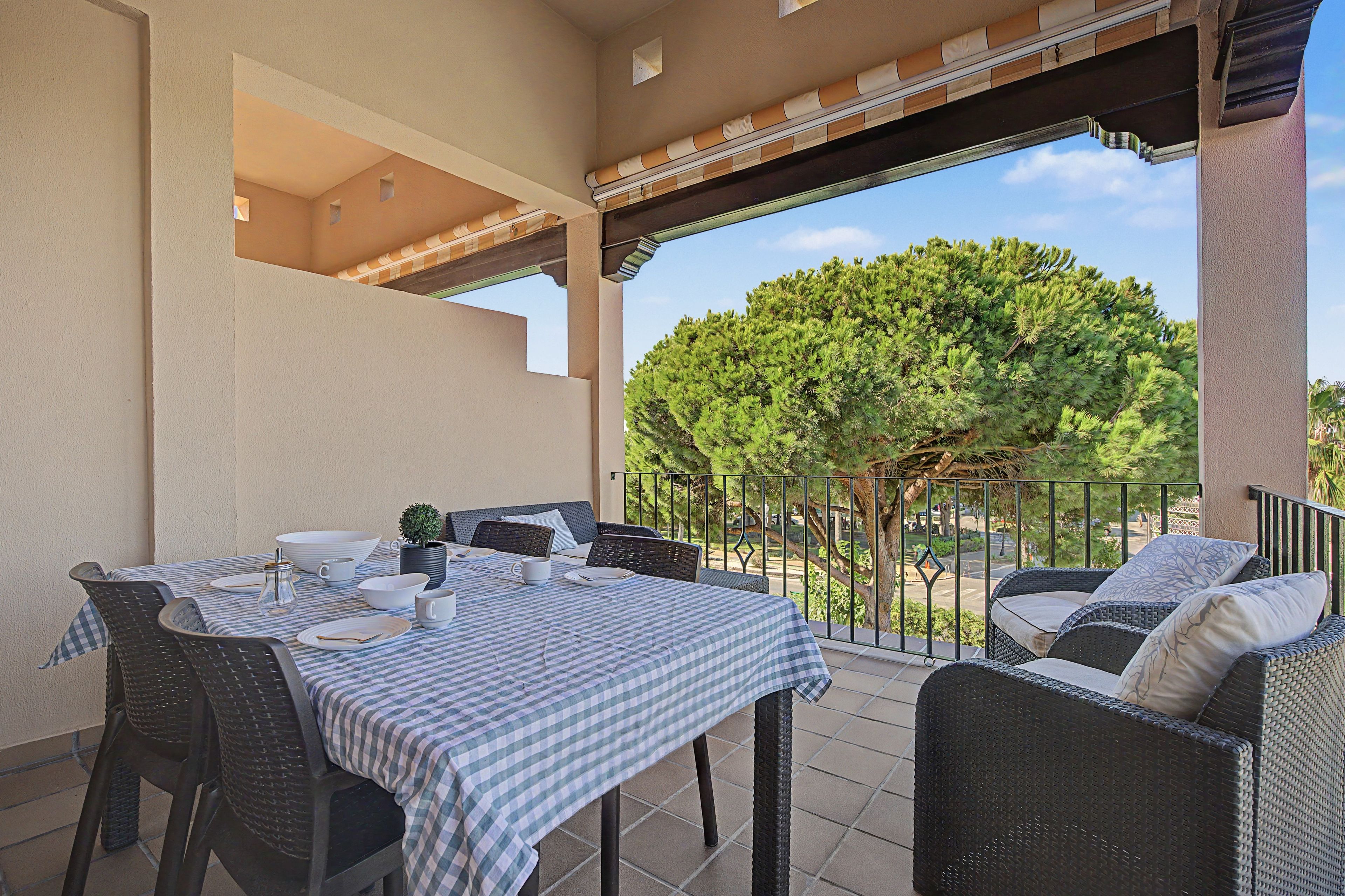 An outdoor patio with a checkered tablecloth, wicker furniture, and a view of a tree.