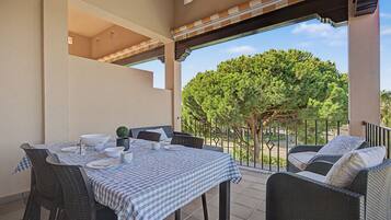 An outdoor patio with a checkered tablecloth, wicker furniture, and a view of a tree.