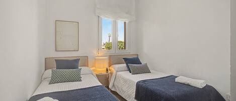 Une chambre double avec deux lits, un ventilateur de plafond, une fenêtre avec vue et une table de chevet avec une lampe.