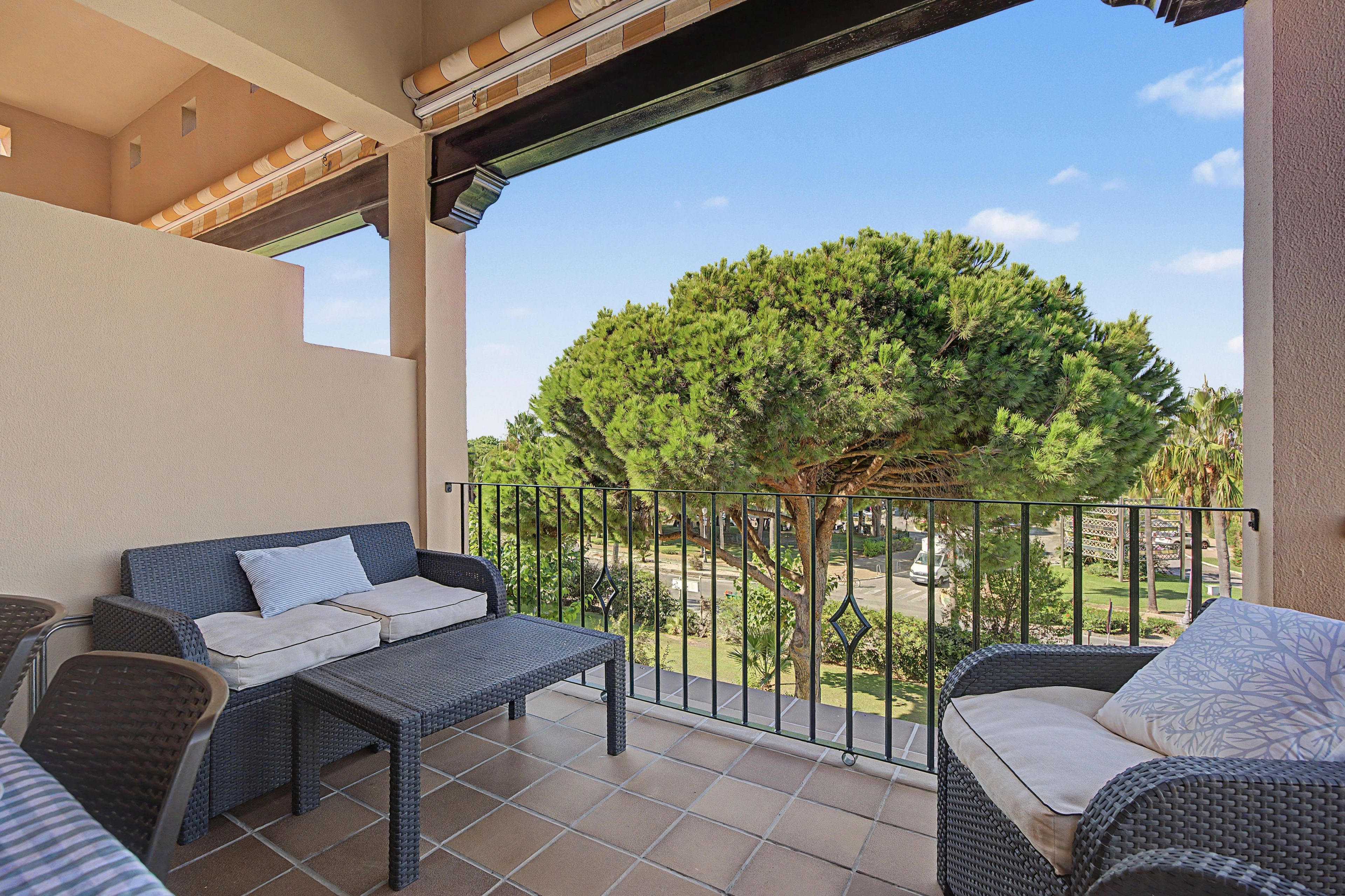 A balcony with wicker furniture, a view of a tree, and a clear sky.
