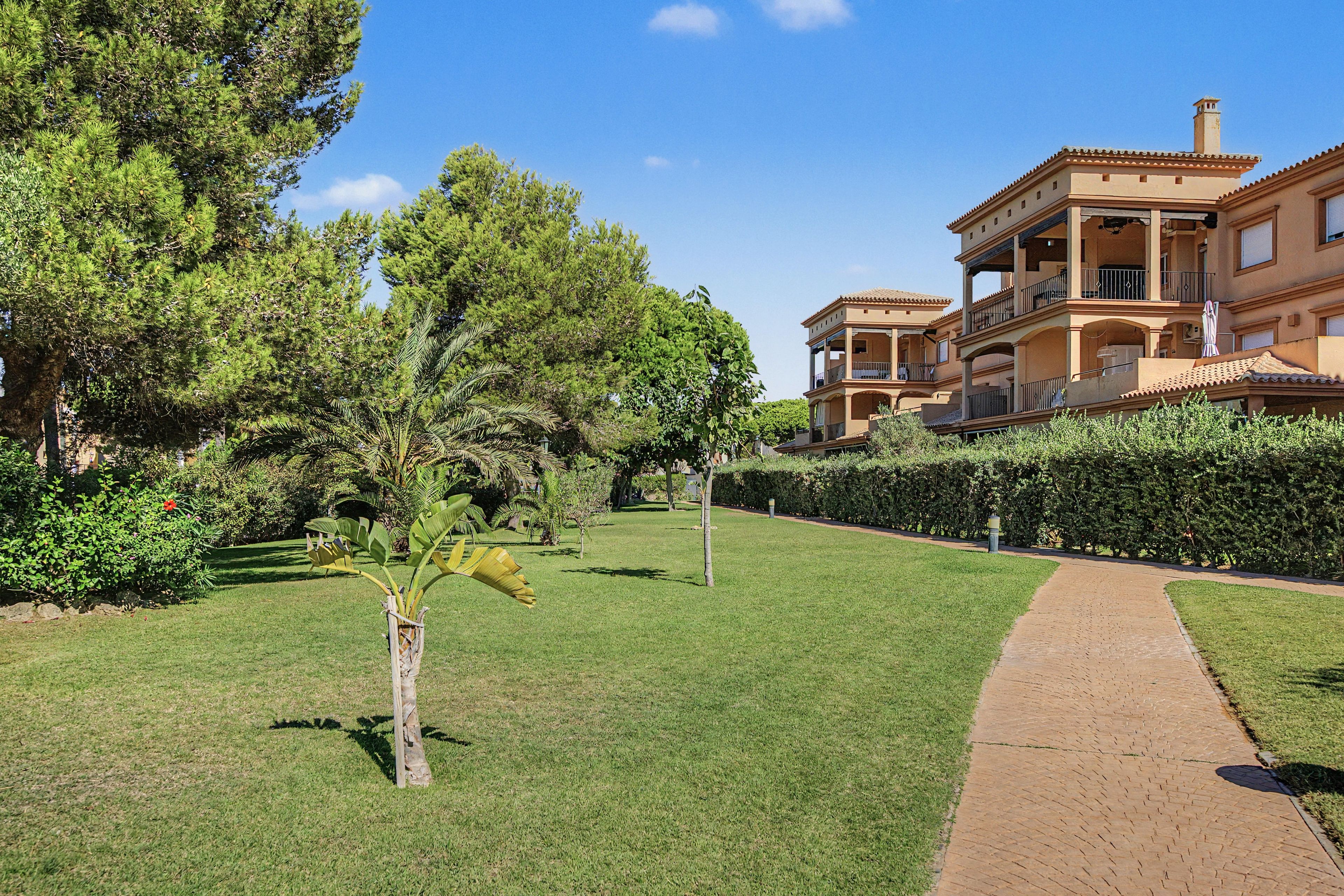 A well-maintained garden with a paved walkway leading to a multi-story building with balconies.