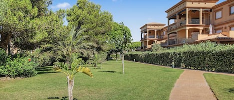 A well-maintained garden with a paved walkway leading to a multi-story building with balconies.