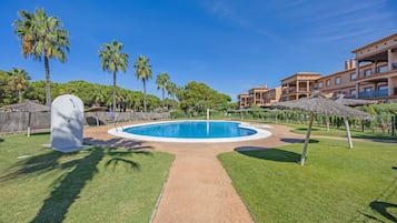 Ein Swimmingpool mit einem Ziegelweg, umgeben von Palmen und einem Gebäude mit Balkonen.