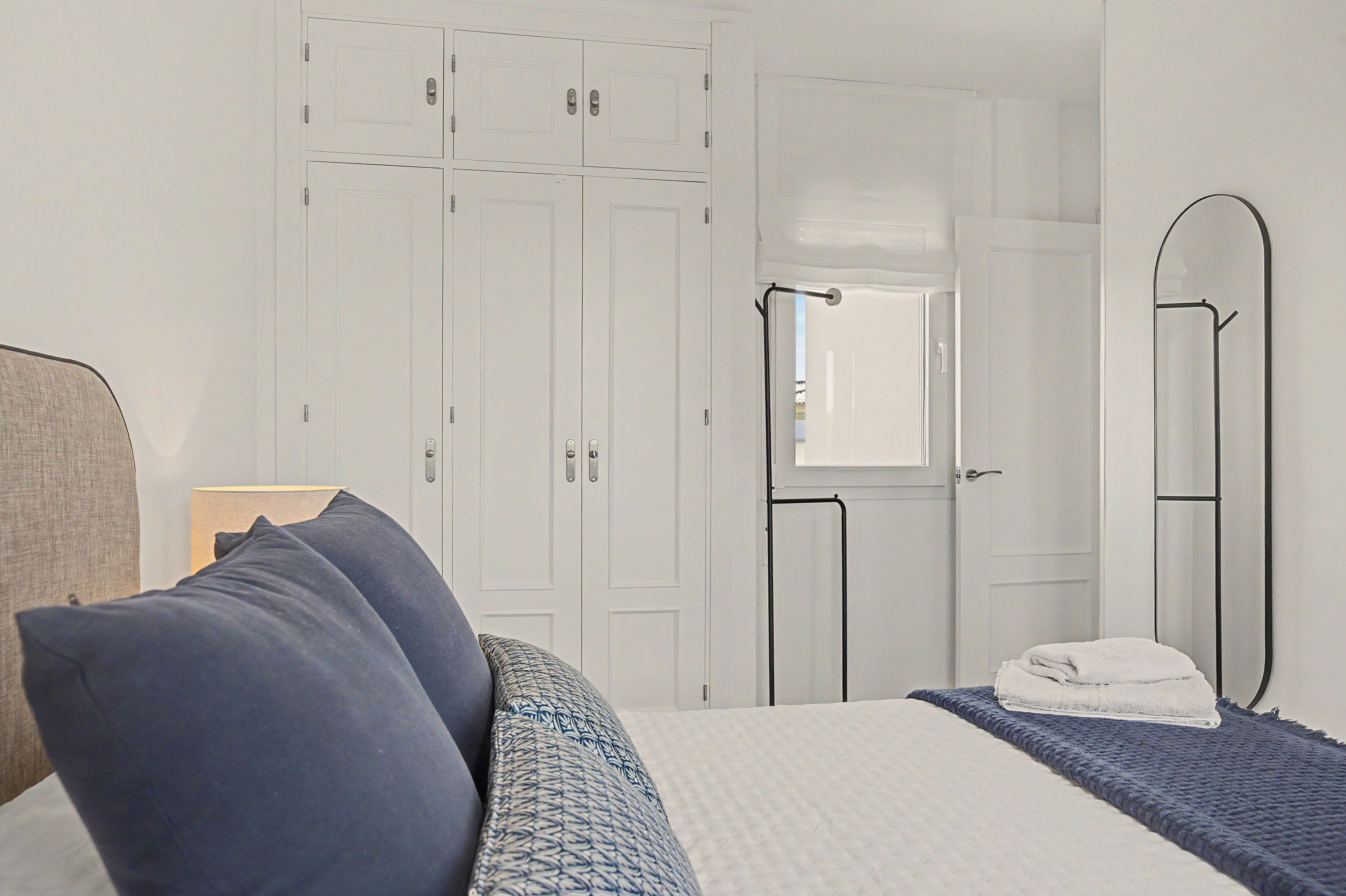Quarto com cama, almofadas, mesa de cabeceira, espelho e guarda-roupa.