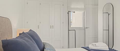 Quarto com cama, almofadas, mesa de cabeceira, espelho e guarda-roupa.