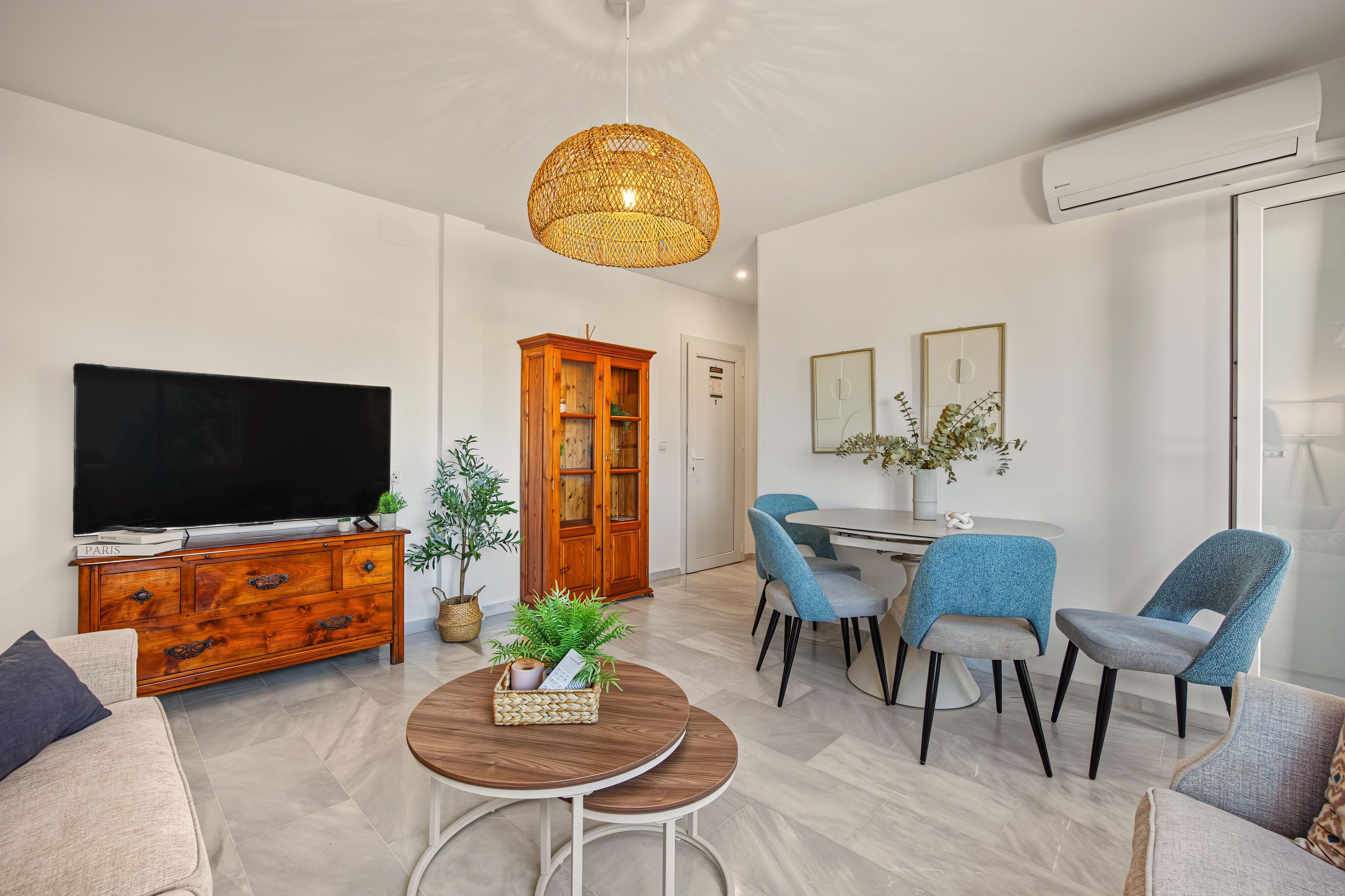 Un salon moderne comprenant un téléviseur, un meuble en bois, une table à manger avec des chaises et un luminaire suspendu.