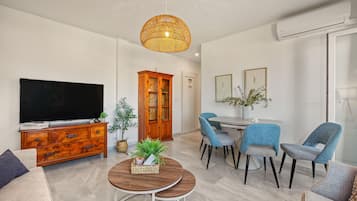 Un salon moderne comprenant un téléviseur, un meuble en bois, une table à manger avec des chaises et un luminaire suspendu.