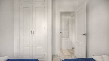 A room with a large wardrobe, a bed with a blue blanket, and a white door leading to another room.