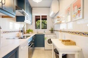 Une cuisine compacte équipée d’un lave-linge, d’un évier et d’une fenêtre donnant sur un espace verdoyant.