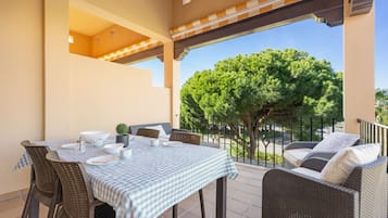 Eine Terrasse mit kariertem Tisch, Korbmöbeln und Blick auf einen Baum.