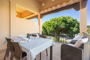 Una terraza con mantel a cuadros, muebles de mimbre y vistas a un árbol.