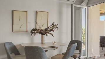 A dining area with a round table, four chairs, two framed artworks, a vase with dried plants, and a sliding glass door leading to an outdoor space.