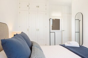 Een slaapkamer met een bed, kussens, een nachtkastje, een spiegel en een garderobe.