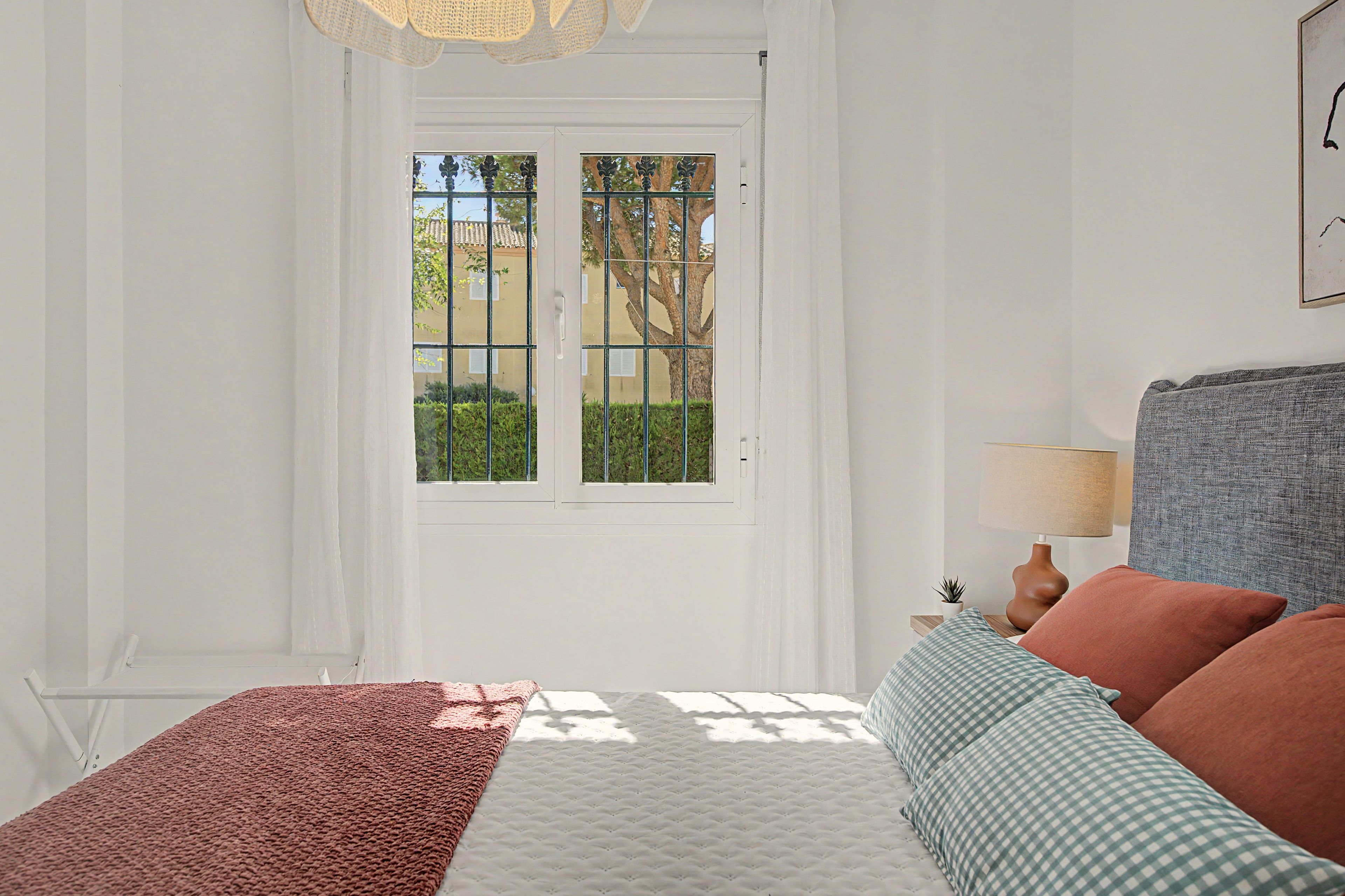 A bedroom with a bed, a nightstand, a lamp, and a view through a window with a door.