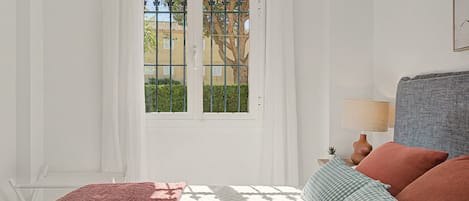 Un dormitorio con cama, mesita de noche, lámpara y vistas por una ventana con puerta.