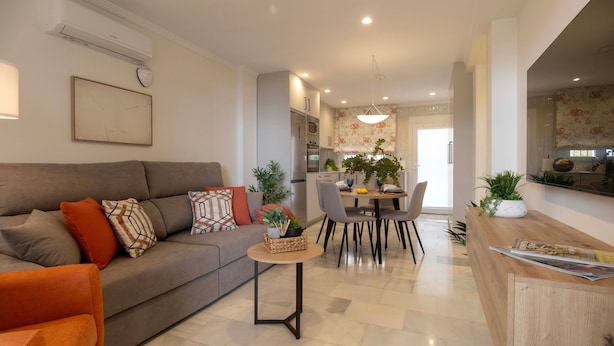 Una sala moderna con un sofá, una mesa de comedor, sillas y una cocina al fondo.