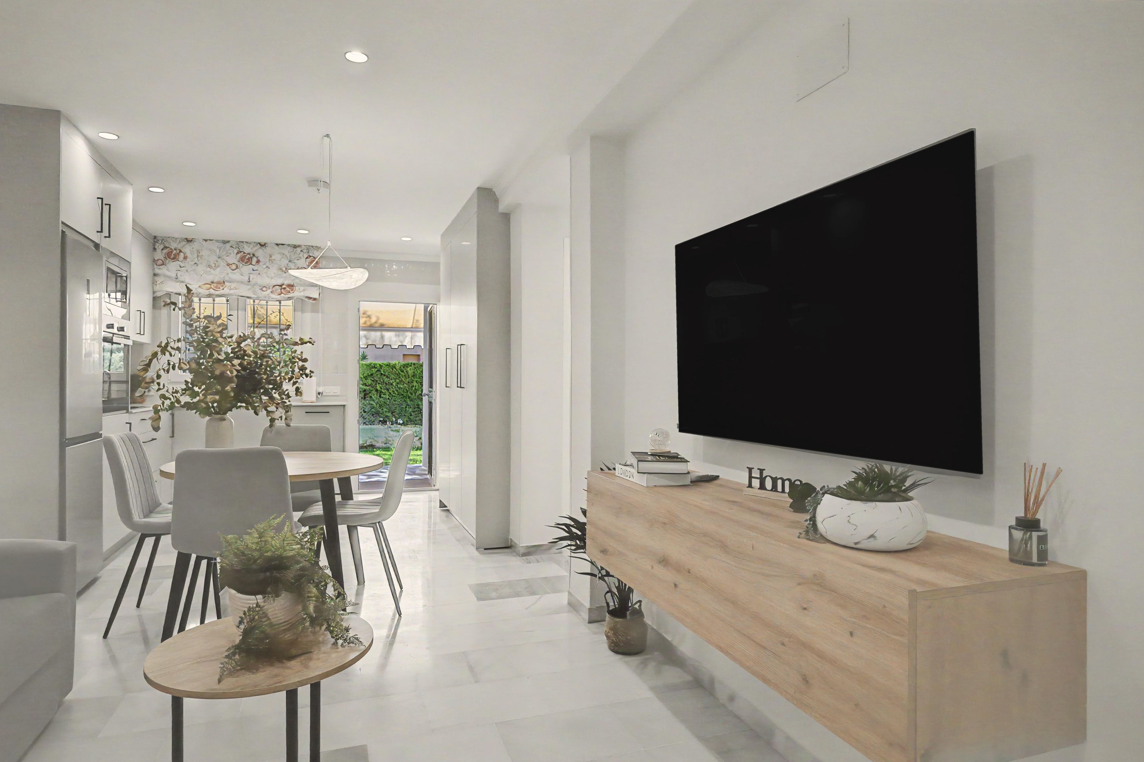 Une cuisine moderne avec un coin repas, un grand téléviseur à écran plat fixé au mur et une console en bois agrémentée d’objets décoratifs.