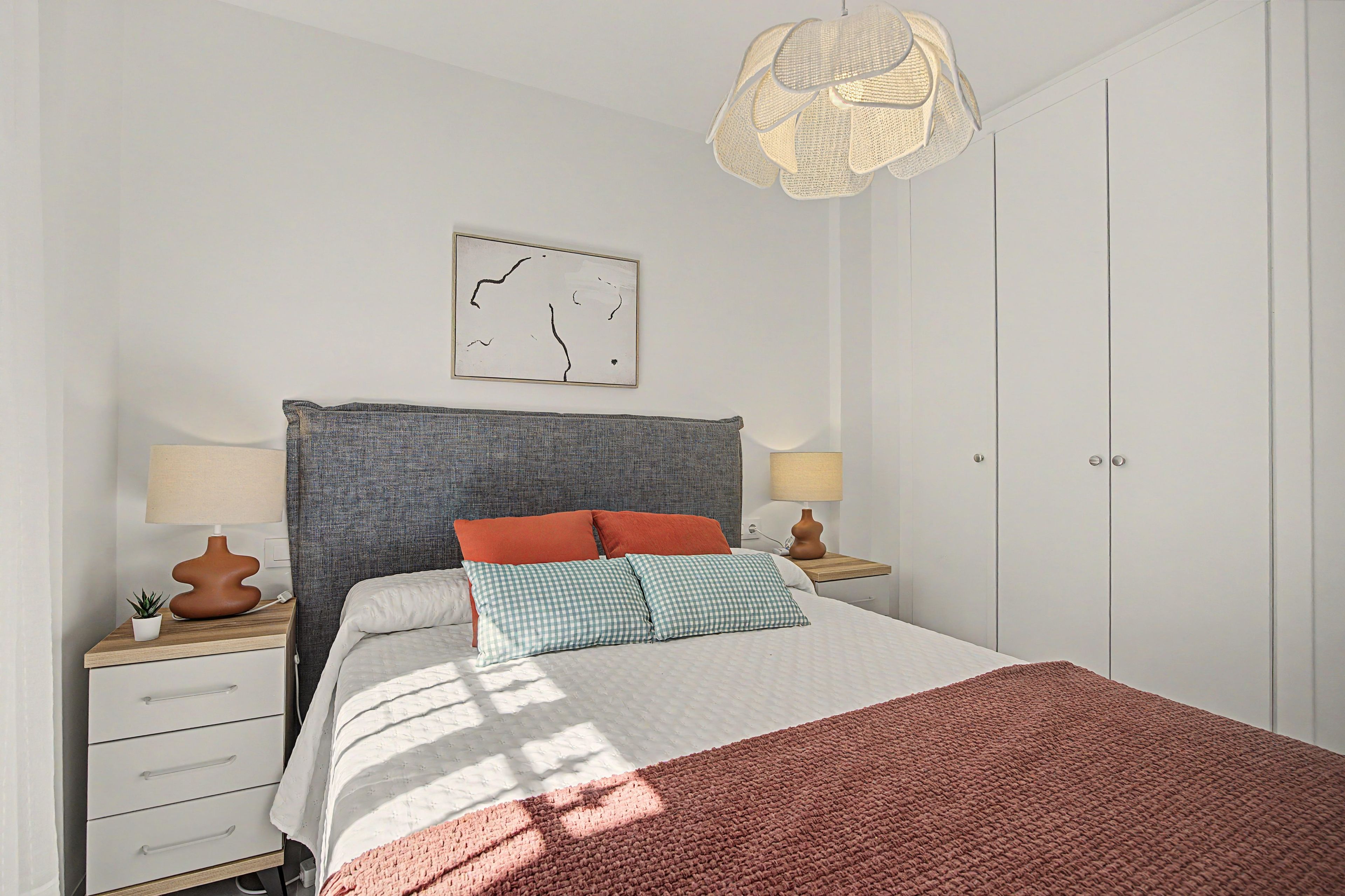 A neatly arranged bedroom with a bed, bedside tables, a hanging light fixture, and a wall-mounted artwork.