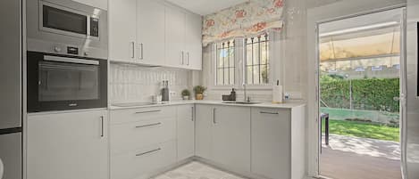 Une cuisine moderne avec des meubles blancs, un four encastré et une fenêtre agrémentée de rideaux décoratifs.