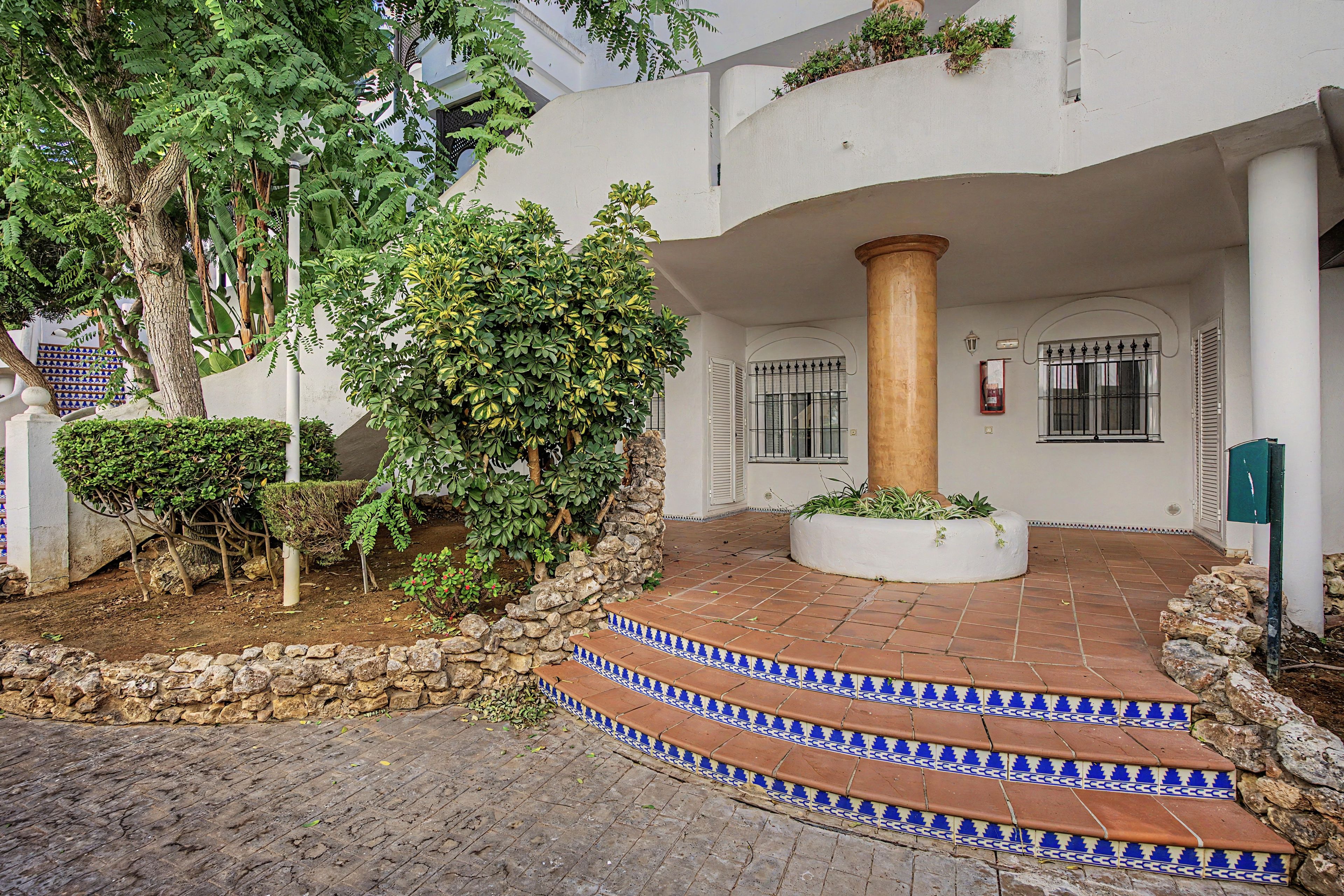 A courtyard with a stone wall, a wooden column, and a tiled staircase leading to a door.