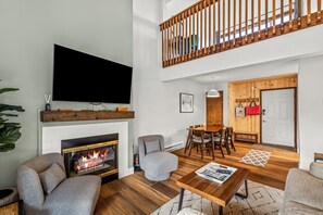 Ein modernes Wohnzimmer mit Kamin, Flachbildfernseher, Essbereich und einer oberen Ebene mit Holzbalkon.