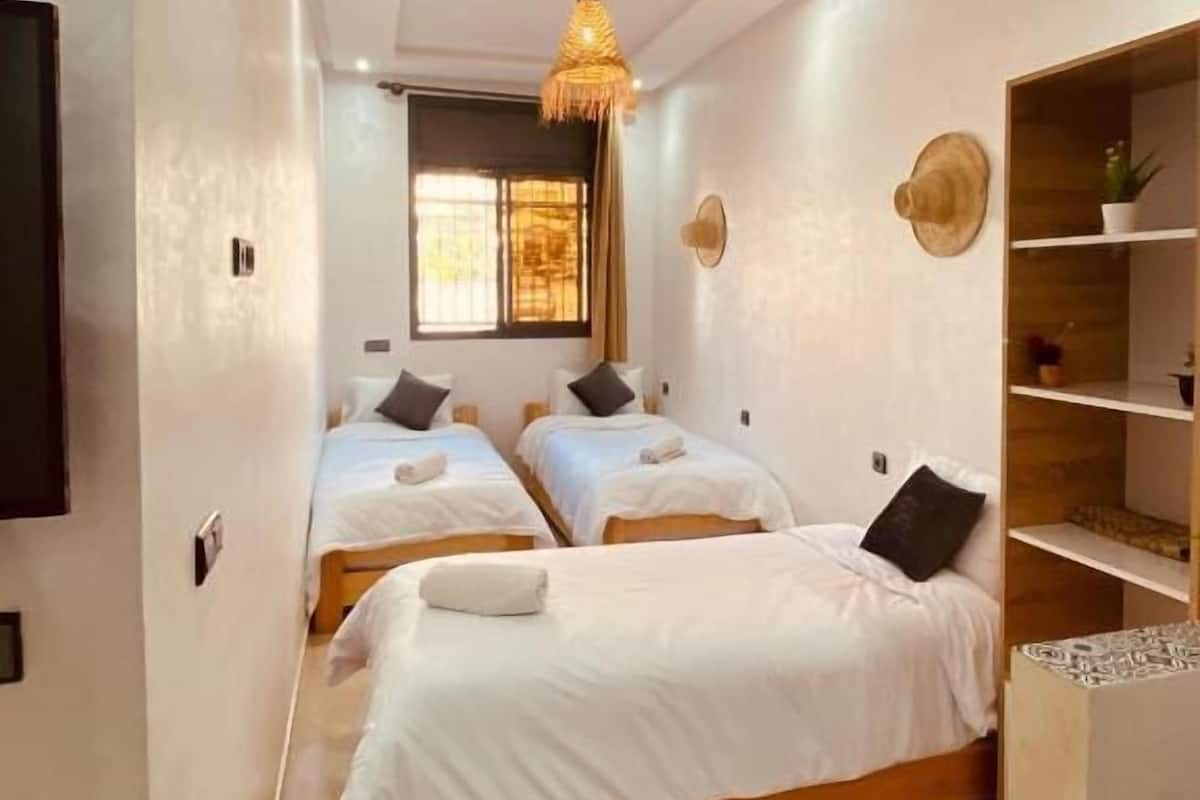 A hotel room with three beds, a TV, a wooden cabinet, and a hanging light fixture.