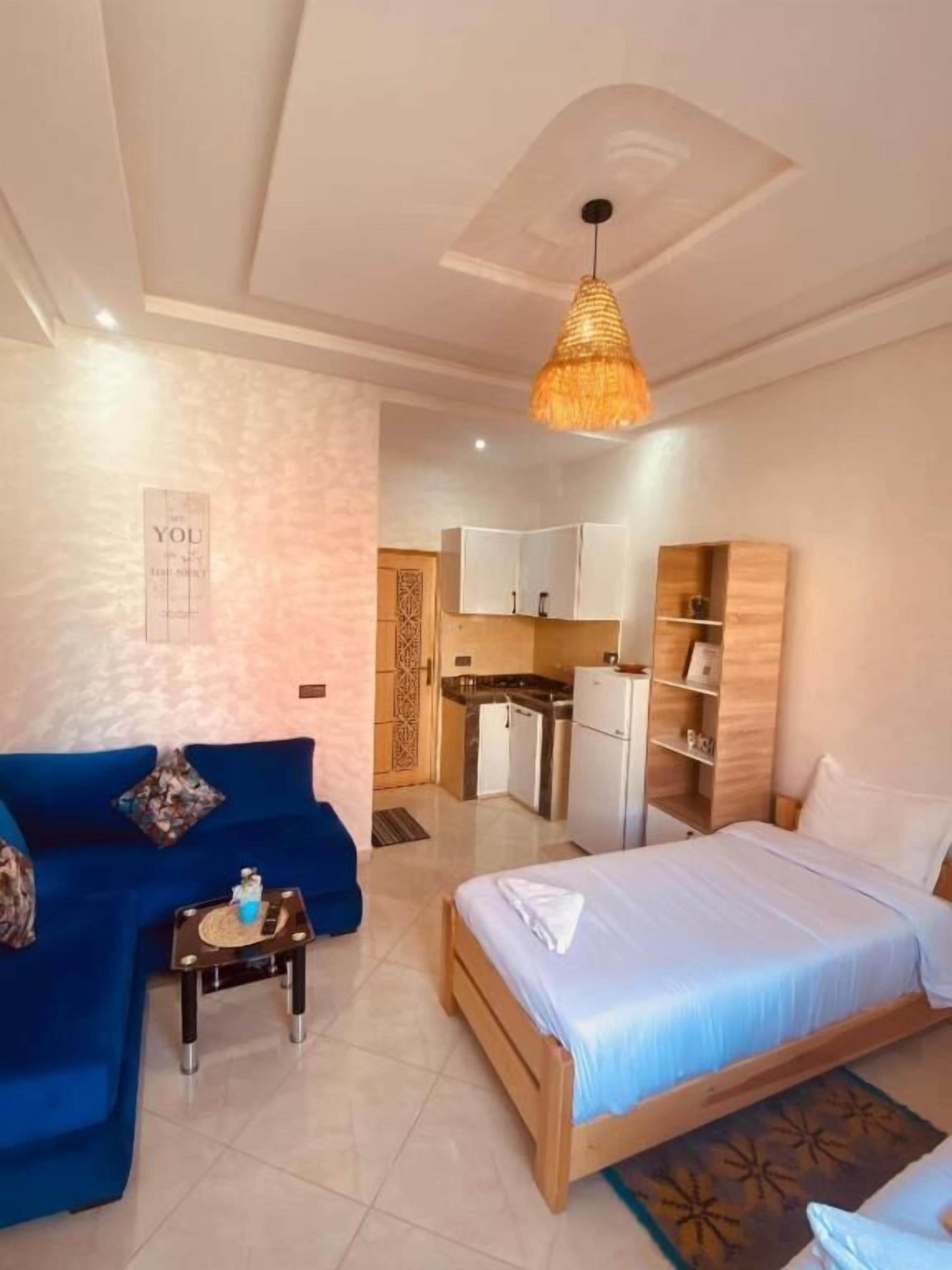 Ein Schlafzimmer mit einem Bett, einem blauen Sofa, einem kleinen Tisch und einer Küchenzeile im Hintergrund.