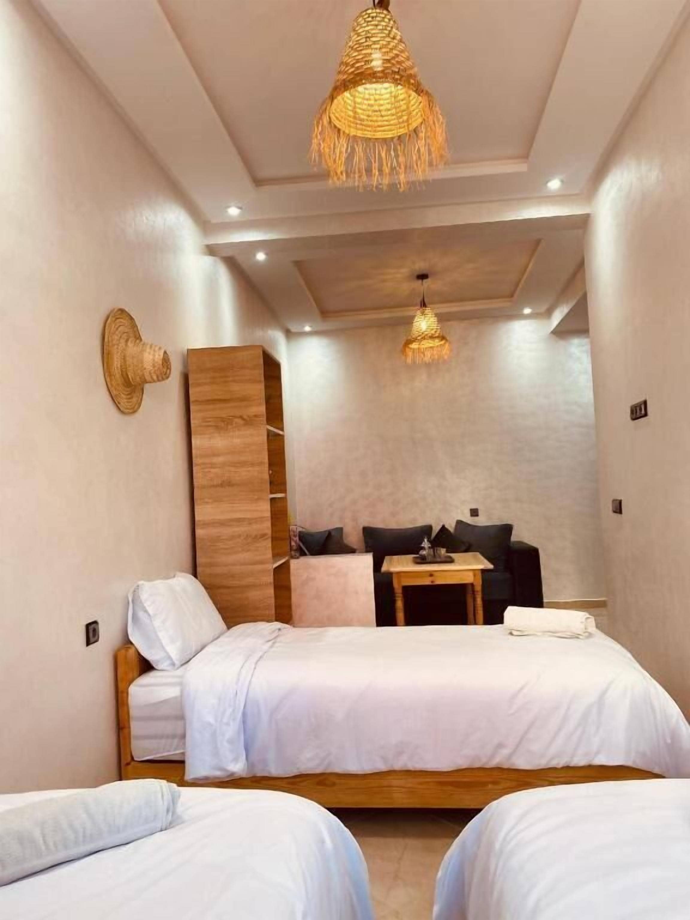 A bedroom with two beds, a wooden wardrobe, a small table, and a hanging light fixture.