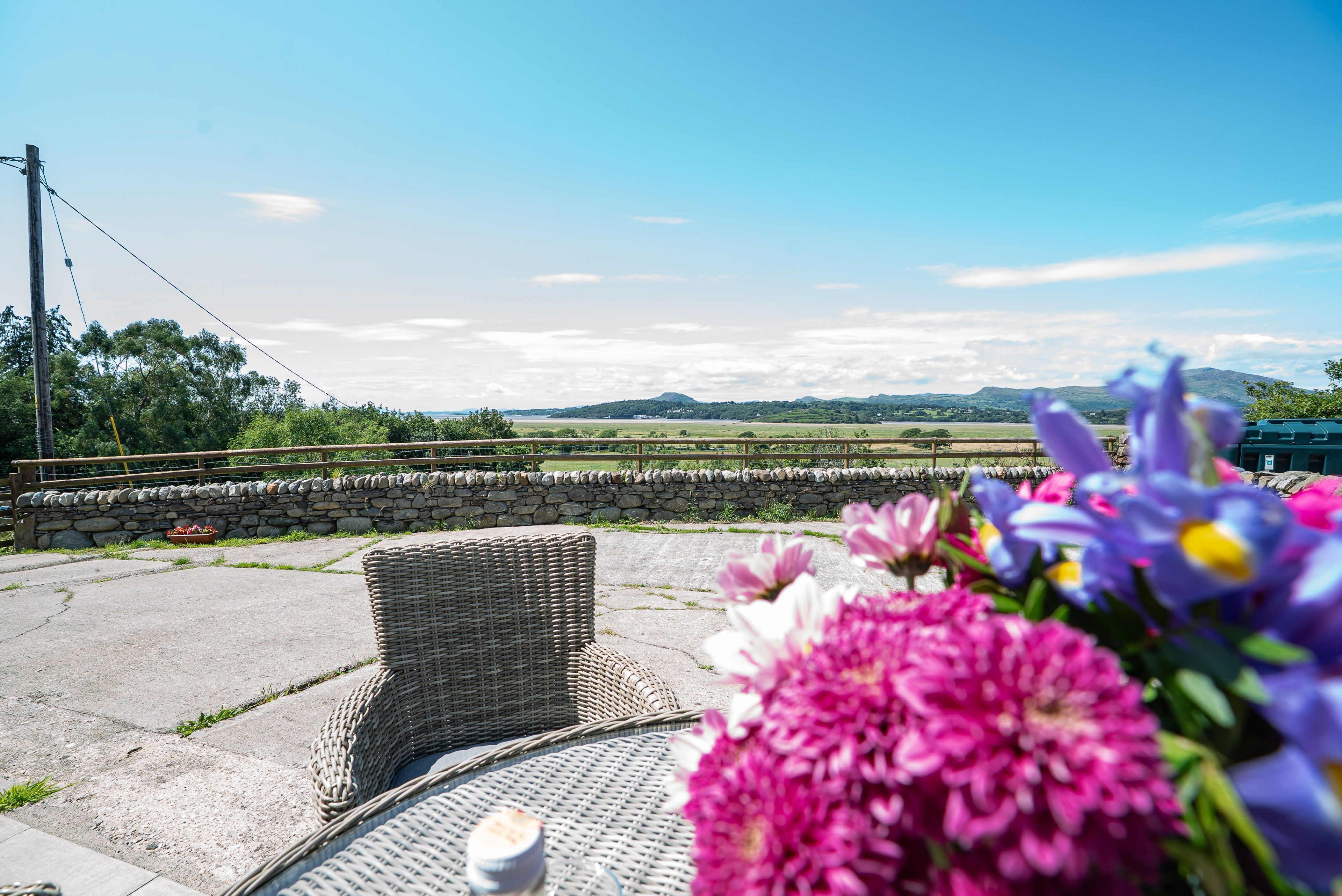 An outdoor seating area with wicker furniture, a stone wall, and a view of the countryside.