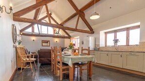A spacious kitchen with wooden beams, a dining table with chairs, a refrigerator, and a window with a view. - Barn stay with Mountain and Estuary views | Beudy-Talsarnau (Talsarnau)