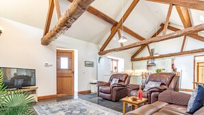 A spacious living room with a large leather sofa, a television, and a wooden ceiling structure. - Barn stay with Mountain and Estuary views | Beudy-Talsarnau (Talsarnau)