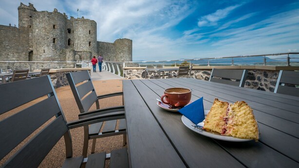 A table with a plate of food and a cup, overlooking a stone wall and a body of water. - Barn stay with Mountain and Estuary views | Beudy-Talsarnau (Talsarnau)